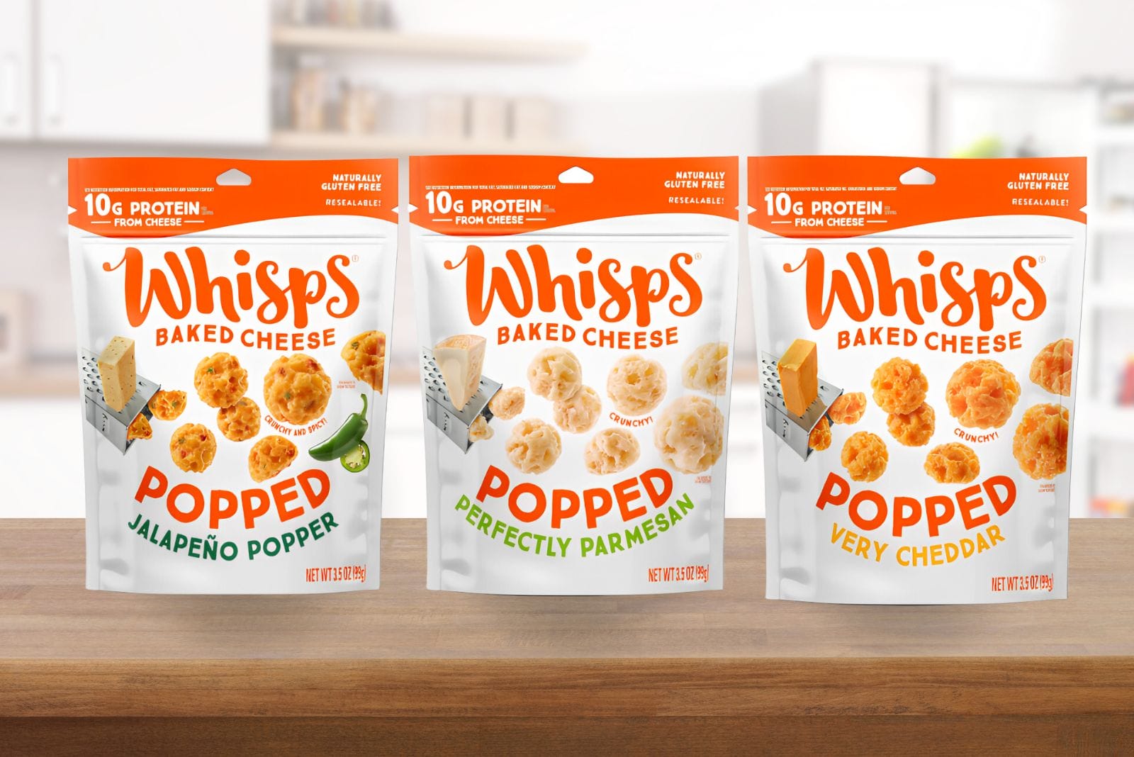 Three packages of Whisps' new baked Popped Chips, in Jalapeno Popper, Perfectly Parmesan and Very Cheddar flavors, sit on a kitchen counter