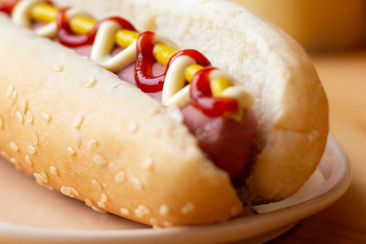 Hot dog in a bun on table covered in ketchup and mustard.