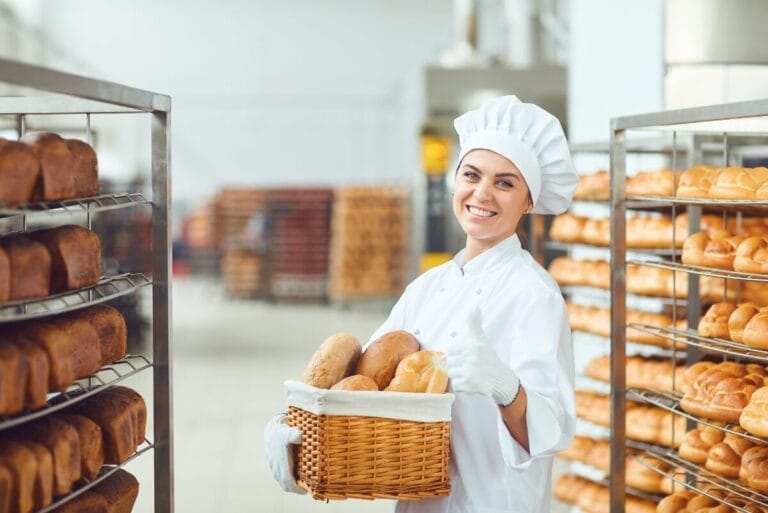 Young baker standing with loaves of bread in a bakery kitchen