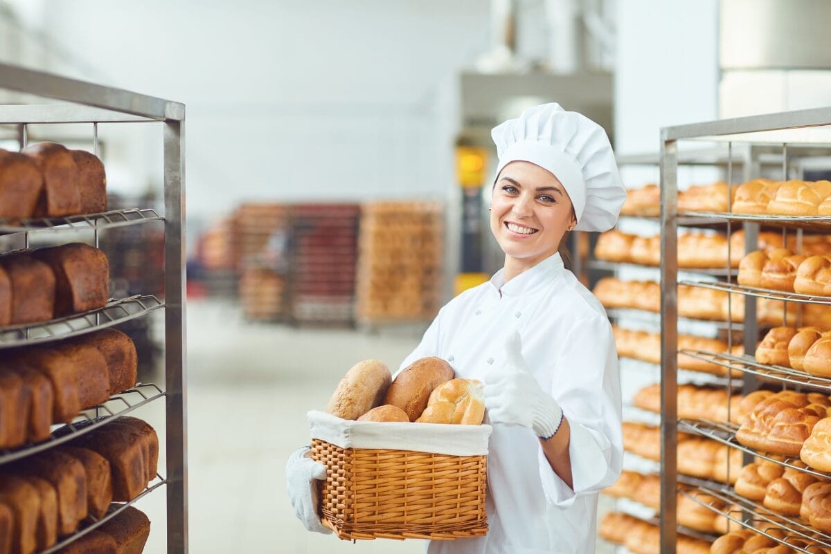 Young baker standing with loaves of bread in a bakery kitchen